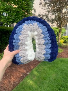 a hand holding up a crocheted blue and white object in front of a house