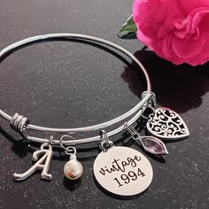 a close up of a bracelet on a table with a flower and a pink rose