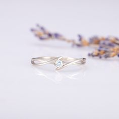 a white gold ring with an aqua blue topazte sits next to lavender flowers