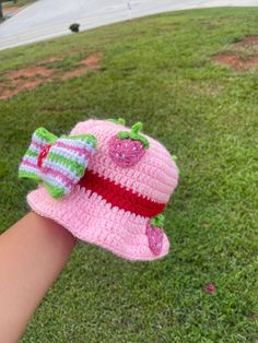 a hand is holding a crocheted hat on the grass