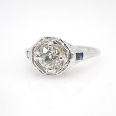 When you picture an "Art Deco" engagement ring, one or two different visions probably pop into your head. At least one of those visions surely resembles this ring.At the center of this 18K white gold ring is a 5mm European Cut diamond (weighing at least half a carat), held in place with four prongs and set into a floating plate gently separated from the rest of the ring. Underneath the center stone is a beautifully crisp filigree pattern reminiscent of a sunrise... and two deep baguette sapphire Octagon Diamond Cut Platinum Ring, Luxury Sapphire Solitaire Ring For Wedding, Heirloom White Gold Octagon Diamond Ring, Heirloom Octagon Diamond Ring In White Gold, White Sapphire Platinum Ring In Fine Jewelry Style, Anniversary Diamond Ring With Single Cut Octagon Diamonds, Heirloom Octagon Diamond Ring For Anniversary, Anniversary Diamond Ring With Octagon Shape, Heirloom Octagon White Gold Diamond Ring