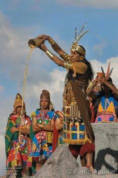 some people dressed in native american clothing and standing on rocks with their hands up to the sky