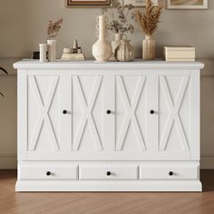 a white cabinet with drawers and vases on top