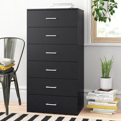 a black dresser with five drawers and a chair next to it in front of a window