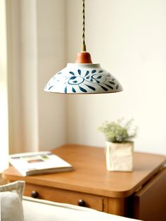 a lamp hanging over a bed next to a wooden table with a potted plant on it