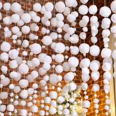 some white balls hanging from the ceiling in front of a brick wall and vase filled with flowers