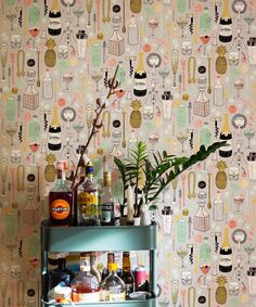 a bar cart with bottles and drinks on it in front of a wallpapered background