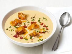 a white bowl filled with soup next to a spoon and napkin on top of a table