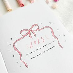 the new year's greeting card is on top of a notebook with pink ribbon