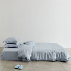 an unmade bed with blue sheets and slippers on the floor next to it