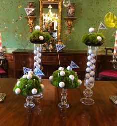 three vases filled with balls and moss on top of a wooden table