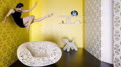 a woman jumping into the air in a room with yellow wallpaper and white furniture