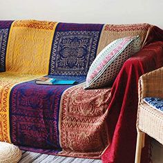 a couch covered in blankets and pillows on top of a wooden floor next to a wicker chair