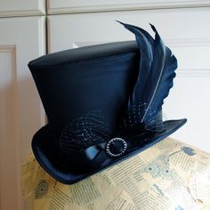 The Liza is a striking cabaret inspired full size top hat. It is covered with beautiful shiny black satin. It is decorated with black ribbon around the crown, black veil, half bow with black crystal buckle and two elegant black goose feathers. Also available as a medium size mini top hat: https://www.etsy.com/listing/256101614/victorian-witch-hatblack-mini-top?ref=shop_home_active_14 Need this TOP HAT in another color?Just send me a message to talk about a custom hat made just for you! This hat Black Gothic Hat For Costume, Vintage Top Hat For Costume Party, Vintage High Crown Top Hat For Costume Party, Vintage Top Hat With Curved Brim For Costume Party, Vintage Curved Brim Top Hat For Costume Party, Gothic Black Top Hat For Costume Party, Steampunk Costume Hat With Curved Brim, Black Gothic Top Hat For Costume Party, Gothic Top Hat With Short Brim For Halloween