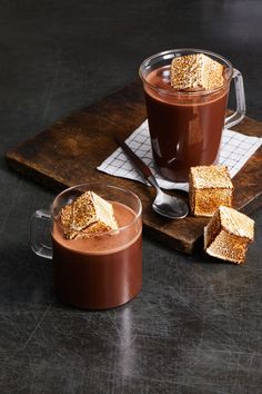 two mugs filled with hot chocolate and marshmallows on a cutting board