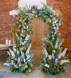 two floral archways in front of a brick wall, with flowers and greenery