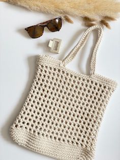 a white crocheted bag next to some sunglasses and a furry animal fur on the floor