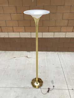 a white and gold lamp sitting on the sidewalk next to a brick wall in front of a building