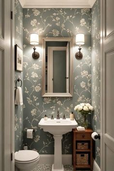 a white toilet sitting under a bathroom mirror next to a sink in a room with blue wallpaper