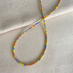 These bright necklaces are made with rainbow seed beads in a randomized pattern, meaning each is unique. They are very dainty and can add a fun but subtle touch to your outfits! Each is handmade with love :) Necklace Length: This necklace is available in lengths of 14, 15, 16, and 18 and inches. If you would like me to add an extender chain on the end of the necklace, please let me know in the personalization box! Note on shipping: The standard shipping for domestic orders is through oversized l Adjustable Playful Beaded Necklaces With Tiny Beads, Playful Beaded Necklaces For Festivals, Yellow Necklaces With Round Letter Beads, Yellow Necklaces With Letter And Round Beads, Yellow Necklace With Letter Beads, Colorful Heart Beads Necklaces For Festivals, Colorful Heart Beads Necklace For Festivals, Rainbow Tiny Beads Necklace For Summer, Colorful Festival Necklaces With Heart Beads