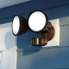 two spotlights on the side of a blue house with white siding and windows in the background