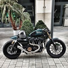 a black motorcycle parked on the side of a street next to palm trees and potted plants