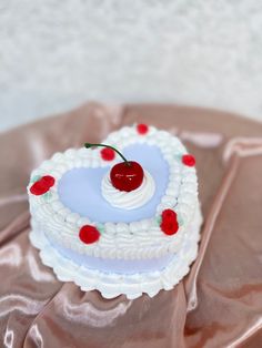 a white cake topped with a cherry on top of a pink satin tablecloth covered table