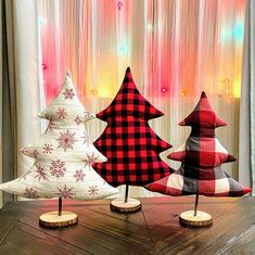 three wooden christmas trees sitting on top of a table next to a window covered in curtains