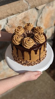 a person holding a cake with chocolate frosting on it