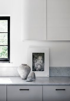 a white vase sitting on top of a counter next to a black and white window