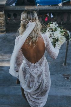 the back of a woman in a white wedding dress holding a bridal bouquet and veil