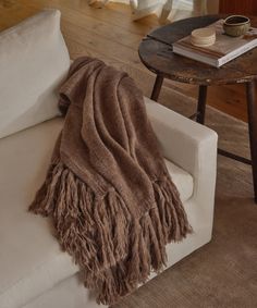 a brown blanket sitting on top of a white couch next to a wooden coffee table