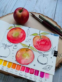 an apple sits on top of a piece of wood next to some markers and pens