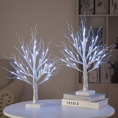 two white lighted trees sitting on top of a table