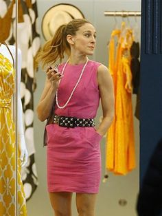 a woman in a pink dress looking at her cell phone while standing next to a mirror