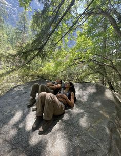 two people sitting on top of a rock in the woods