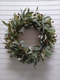 a green wreath hanging on the side of a white wall with red berries and leaves