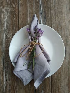 napkins with lavender flowers tied to them on a white plate against a wooden background