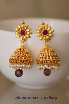 Grand and beautiful metal work jhumka earrings! The body of the jhumka sports a grand and intricate metal work, while the post of the earrings has a simple sun emblem with a pinkish purple kundan stone studded in the center. A cluster of small white pearls dangle from the rim.  A light colored purple stone hangs from the jhumka amongst a cluster of white beads. Earrings measure 2 3/4 inches (7 cm) in length. The earrings are made of copper metal with one gram gold plating. JEWELERY CARE INSTRUCT Temple Style Dangle Jhumkas, Temple Jewelry Style Jhumkas For Navratri, Temple Jewelry Jhumkas For Navratri, Temple Style Drop Jhumkas For Navratri, Temple Style Jhumkas For Navratri, Wedding Jhumkas With Latkans, Wedding Drop Jhumkas With Latkans, Wedding Drop Jhumkas, Intricate Design Jhumkas For Puja