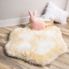 a stuffed animal sitting on top of a wooden floor next to a rug and pillow