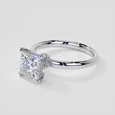 a white gold ring with a princess cut diamond in the center, on a plain surface