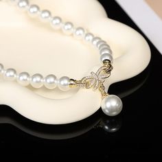 Embark on a journey of sophistication with our Bridal Pearl Earring and Necklace Set, where timeless elegance meets modern sparkle. This exquisite pearl jewelry set centers around a 10mm white pearl, renowned for its classic beauty and radiant glow. Representing centuries of elegance, the pearl is perfectly complemented by the set's contemporary design, making it an ideal choice for brides or anyone looking to add a touch of refined glamour to their ensemble. Delicate Glamour: Chic Bow Pendant O Elegant White Jewelry With Pearl Charm, Elegant White Pearl Necklace With Charm, Elegant Formal Jewelry Sets With Pearl Pendant, Pearl Jewelry Sets With Pearl Chain, White Pearl Necklace With Elegant Design, Elegant Pearl Pendant Jewelry Set For Formal Occasions, Formal Pearl Jewelry Sets With Elegant Design, Formal Pearl White Bracelet With Pearl Pendant, Elegant Pearl Drop Jewelry Set