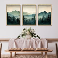 three paintings hang on the wall above a table with a vase filled with flowers and greenery