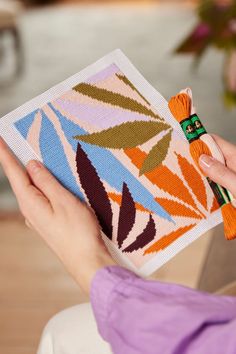 a woman is holding a needle case with an orange and green flower design on it