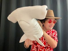 a man in a red shirt and hat holding a large white shark balloon with his mouth open