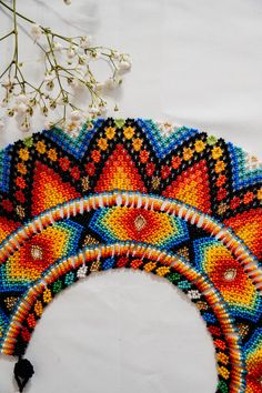 three colorful beaded designs on a white surface next to some flowers and branches with leaves