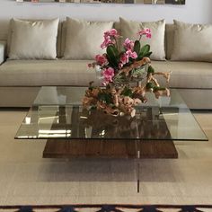 a glass coffee table with flowers on it in front of a couch and mirror wall