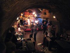 a group of people are gathered in a dark room with exposed ceilings and stone walls