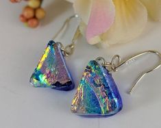 a pair of blue earrings with iridescents on them sitting next to a flower