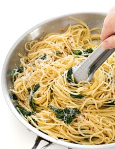 someone using a spatula to stir pasta in a pan with spinach and cheese